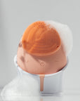 Beauty device with orange bristle head and white base on a gray background