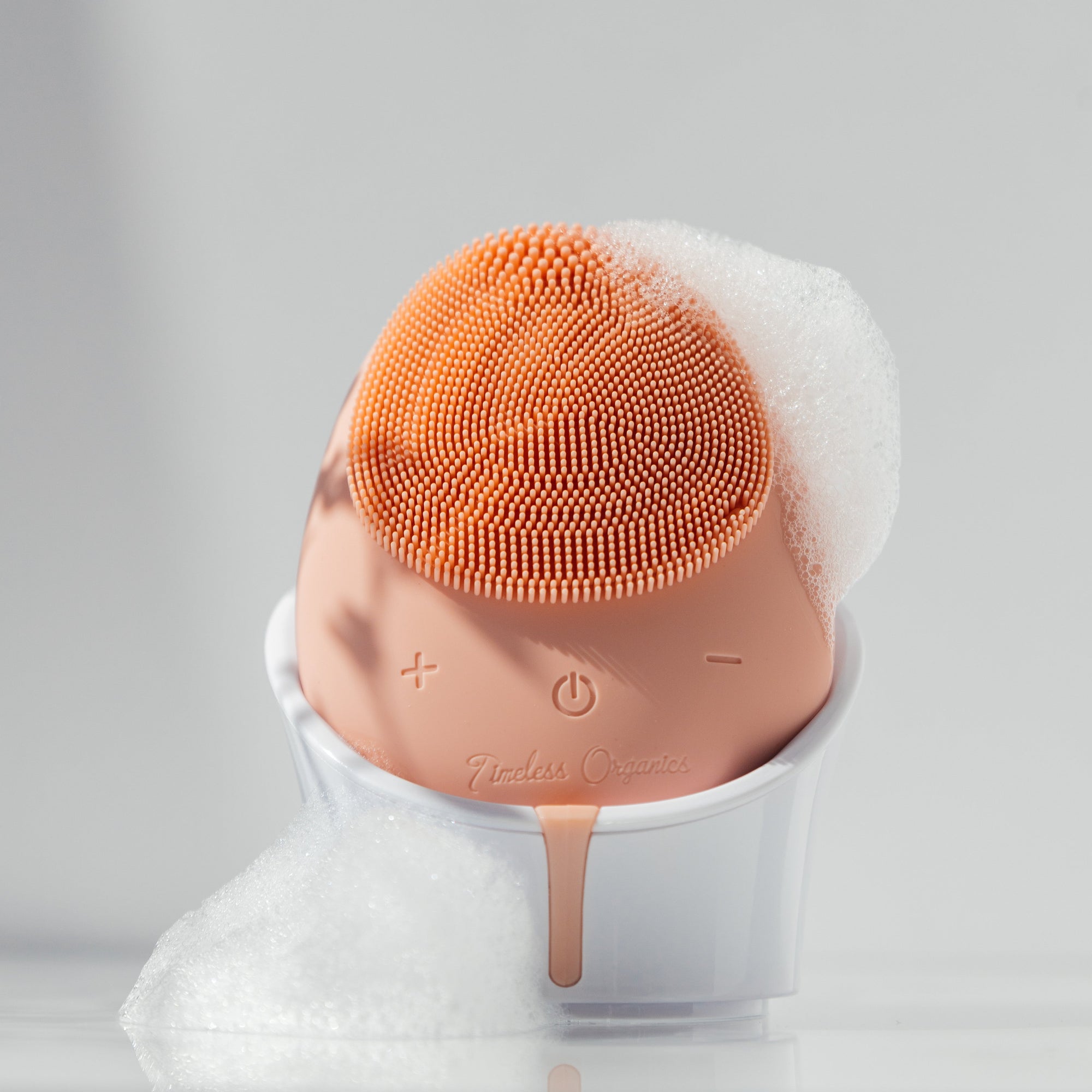 Beauty device with orange bristle head and white base on a gray background